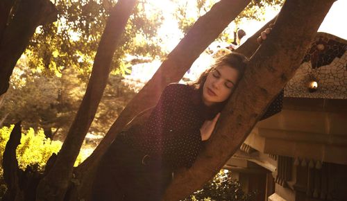 Young woman looking away while standing on tree trunk