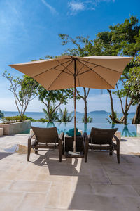 Chairs and tables by swimming pool against sky