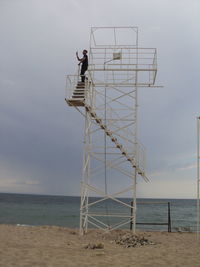 Low angle view of mid adult man standing on lookout tower at sandy beach