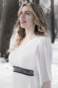 Smiling young woman looking away while standing on snow covered field