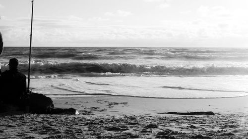 Silhouette man sitting at beach against sky