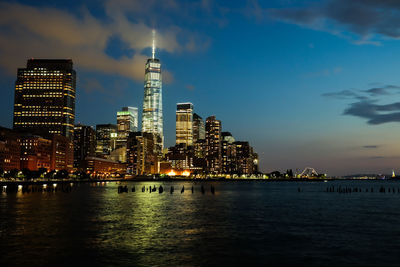 Scenic view of sea by illuminated cityscape against sky at dusk