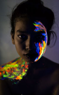 Close-up portrait of young woman with face paint in darkroom