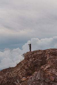 Full length of boy standing by cliff while holding camera against sky