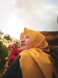 Side view of woman holding yellow flowering plant