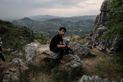 Side view of young man on rock against mountains