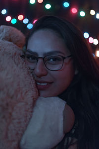 Close-up portrait of young woman with teddy bear against illuminated lights