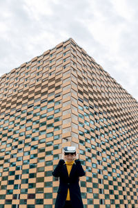 Female in jacket and turtleneck using vr goggles near building windows in daylight