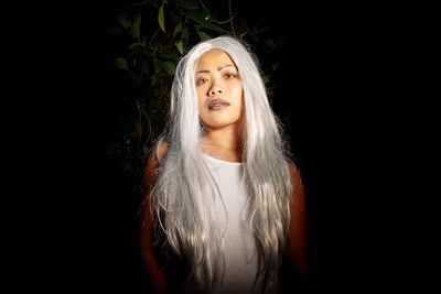 Portrait of young woman with long white hair standing at night