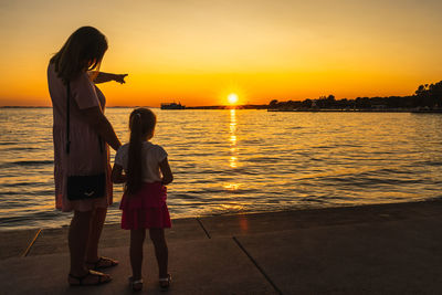 Women standing on sea against sky during sunset