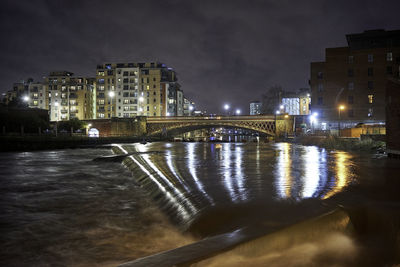 Illuminated bridge over river by buildings in city at night