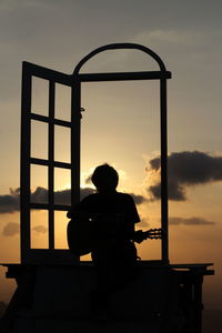 Rear view of silhouette boy sitting against sky during sunset