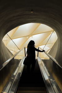 Woman standing on escalator against patterned ceiling