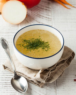 Healthy bone broth in a bowl with dill on a light wooden background.