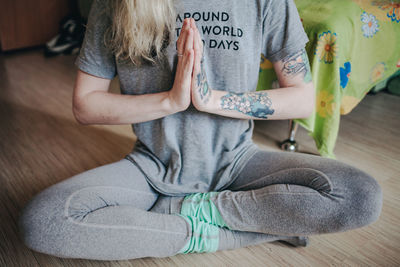 Low section of woman meditating while sitting on floor at home