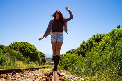 Full length of young woman standing on railroad track against sky