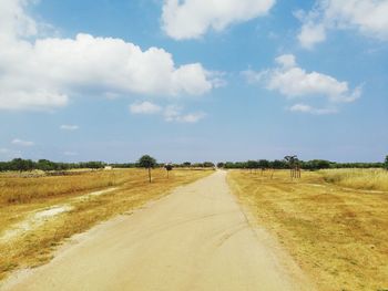 Dirt road amidst field against sky