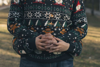 Midsection of father with son holding burning sparkle while standing on field