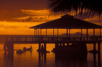 Pier with gazebo on sea against sky during sunset