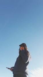 Low angle view of woman standing against blue sky