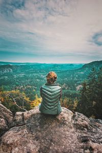 Rear view of woman sitting on mountain against sky