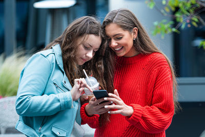 Two girlfriends use a smartphone, laugh and talk, technology concept with always connected milenials