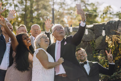 Happy newlywed senior couple taking selfie with family and friends through smart phone