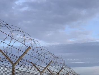 Low angle view of barbed wire fence against sky