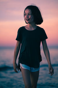 Young woman standing against sea during sunset