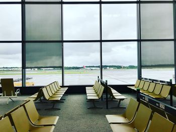 Empty chairs against sky seen through glass window