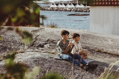 Male siblings looking away while sitting on blanket over archipelago during weekend