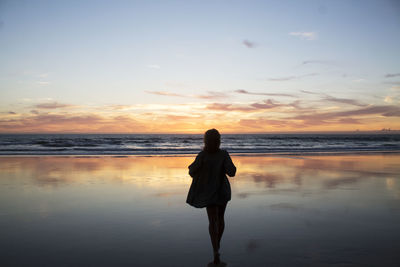 Rear view of young woman walking towards shore during sunset