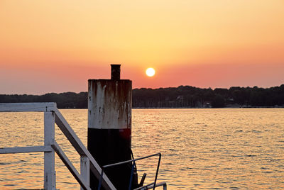 Wooden posts in sea against sky during sunset