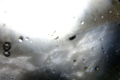 Close-up of wet window against sky during winter