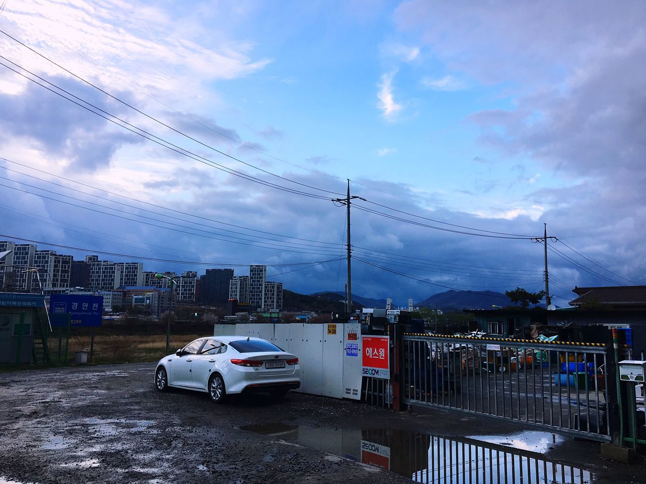 cloud - sky, sky, mode of transportation, transportation, car, motor vehicle, city, architecture, electricity, built structure, land vehicle, building exterior, nature, cable, road, power line, street, technology, no people, connection, outdoors, power supply