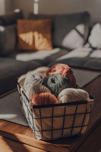 Balls of earth coloured yarn inside a basket on a table inside an apartment.