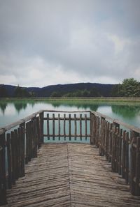 Pier on lake against cloudy sky