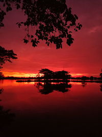 Silhouette trees by lake against romantic sky at sunset