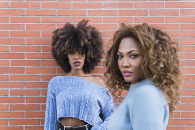 Attractive african american women with long afro hair and blue shirt posing in brick wall