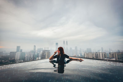 Full length of man with arms raised in city against sky