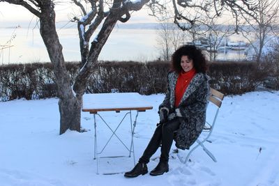 Woman sitting on chair against trees during winter