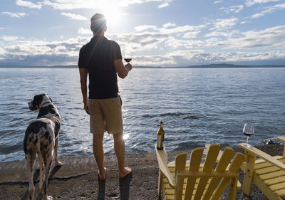 Rear view of man with dog standing in sea against sky