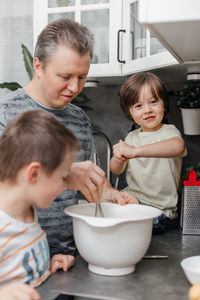 Caucasian dad with two children preparing dough for a pie or biscuit in the kitchen at home. 