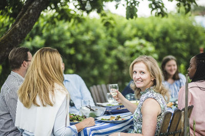 Smiling woman holding wine glass while sitting with friends at garden party