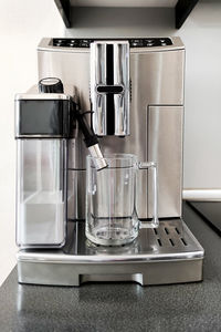 Steel-colored coffee machine for making different types of coffee with glass cup on stand. 