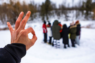 Cropped hand of man gesturing against crowd of people during winter