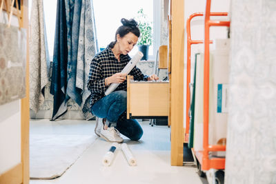 Full length of saleswoman arranging wallpaper in drawer