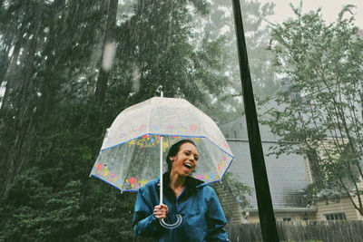 Happy woman holding umbrella during rainfall
