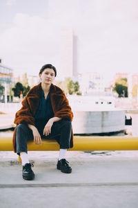 Full length of young woman sitting on pole against sky