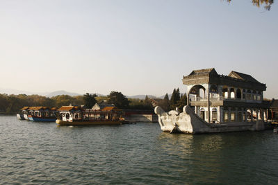 Boats in river by buildings against clear sky